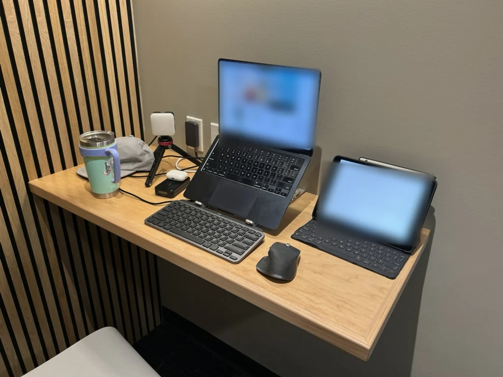 Marcus's setup before M∆NTLE: a laptop on a stand, an iPad with keyboard, a separate keyboard and mouse, a light on a mini tripod, a charger and cables on a small desk
